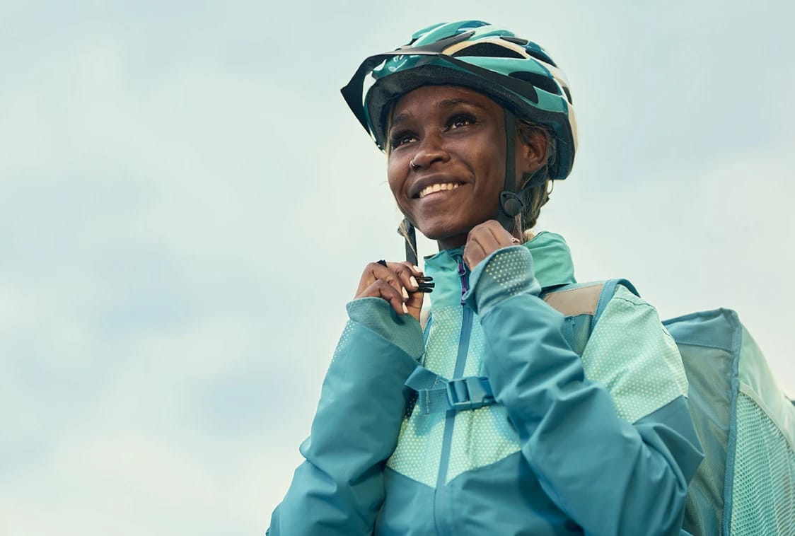 A smiling cyclist adjusts her helmet straps before riding.