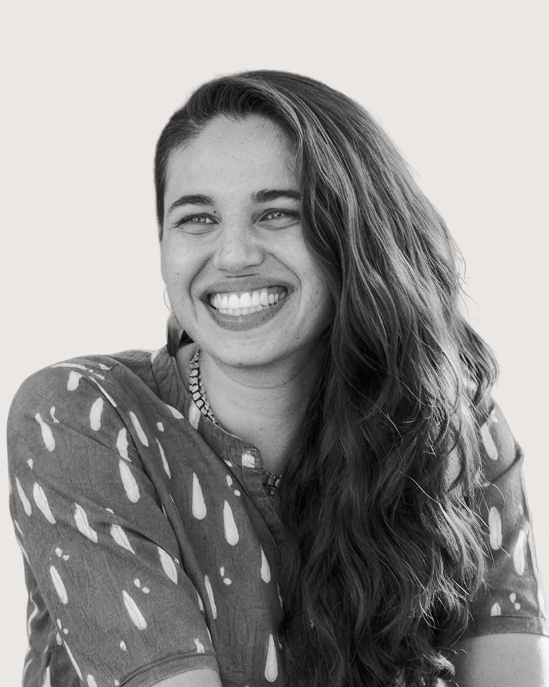 Smiling person with long hair wearing a patterned top, shown in black and white.