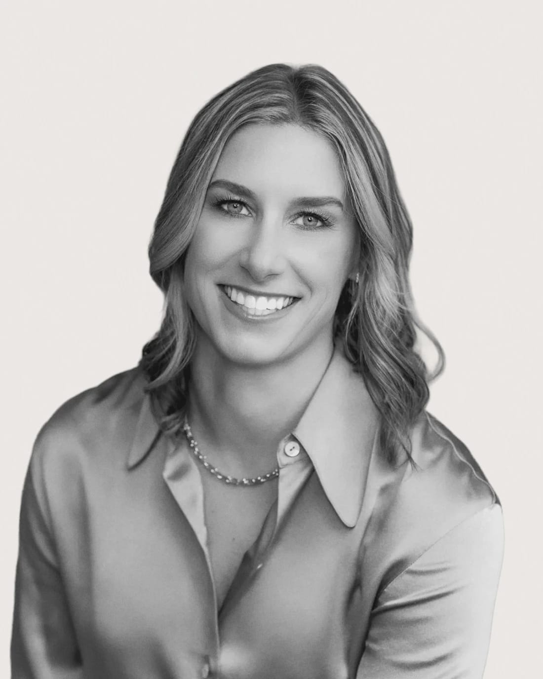 Smiling woman with shoulder-length hair wearing a collared blouse and necklace.