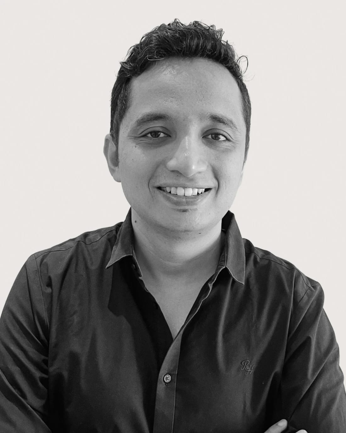 Smiling man with short dark hair wearing a black collared shirt.