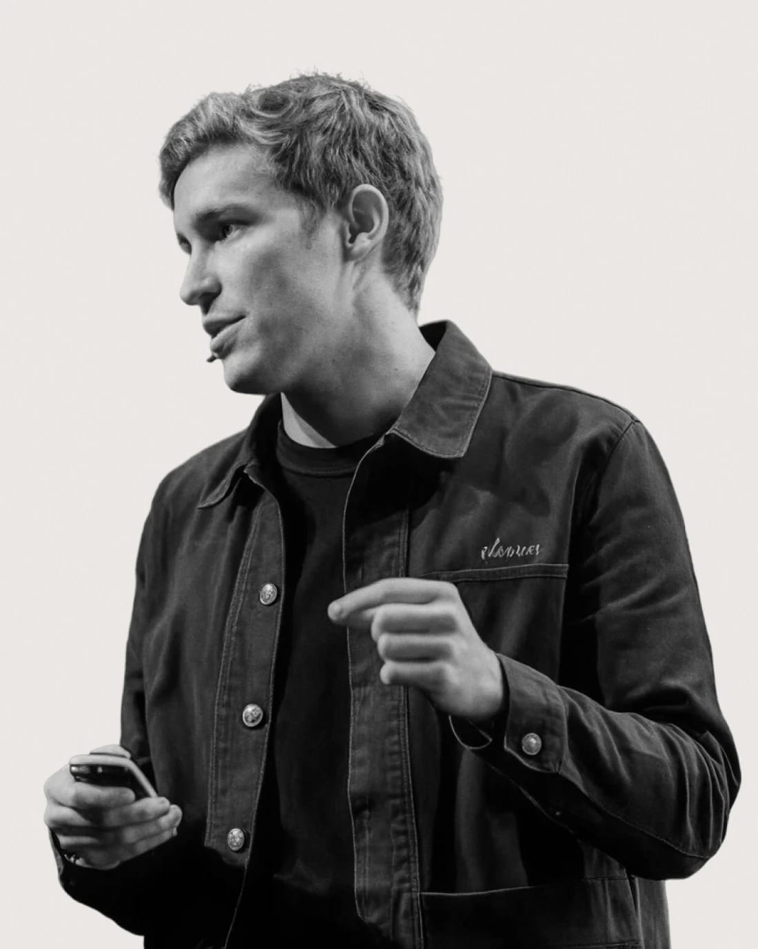 Young man holding a smartphone, wearing a dark jacket and looking to the side.