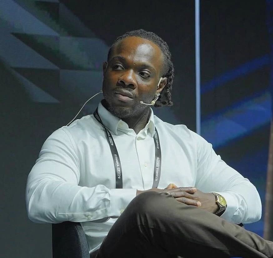 Chibuzor Oluo in a white shirt and headset seated onstage during a conference.