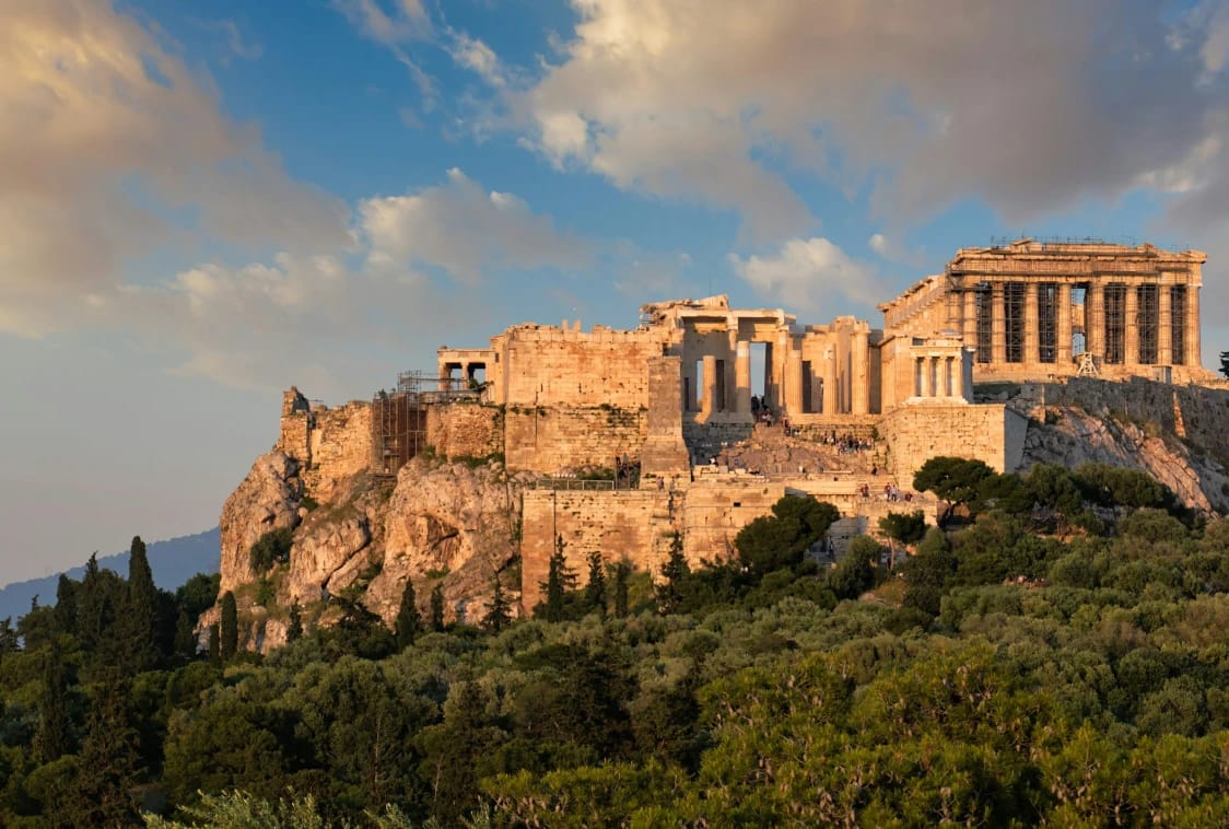 The Acropolis of Athens, including the Parthenon, illuminated above the surrounding greenery.