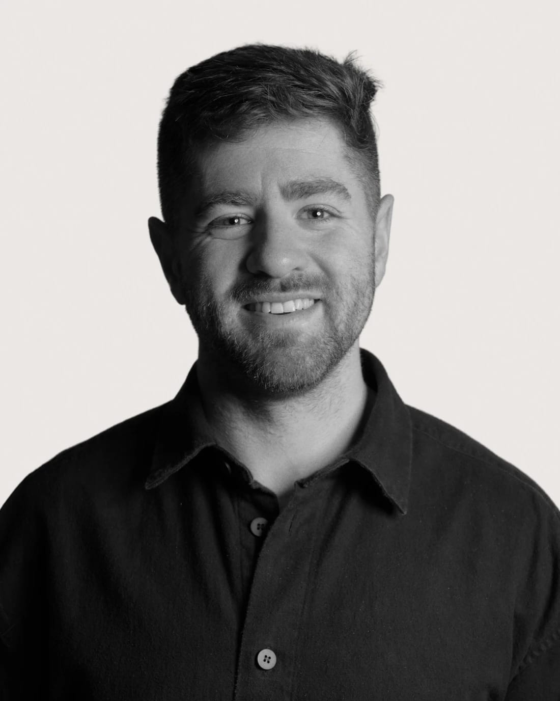 Smiling bearded man in a black collared shirt, facing the camera.