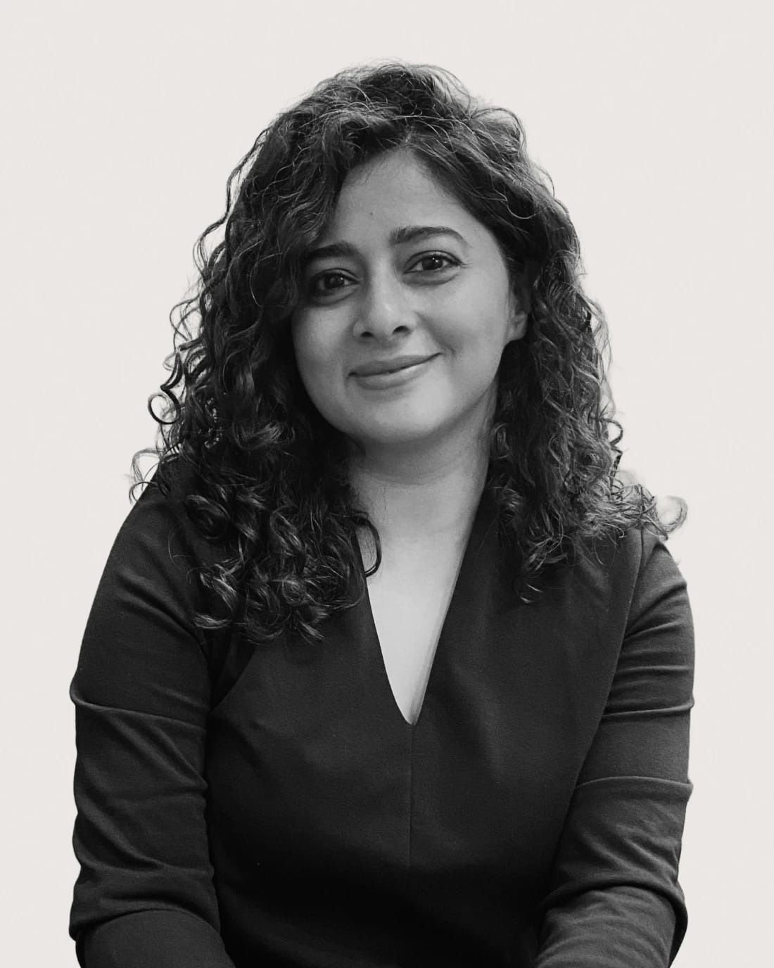 Black-and-white portrait of a smiling woman with curly hair wearing a dark blouse.