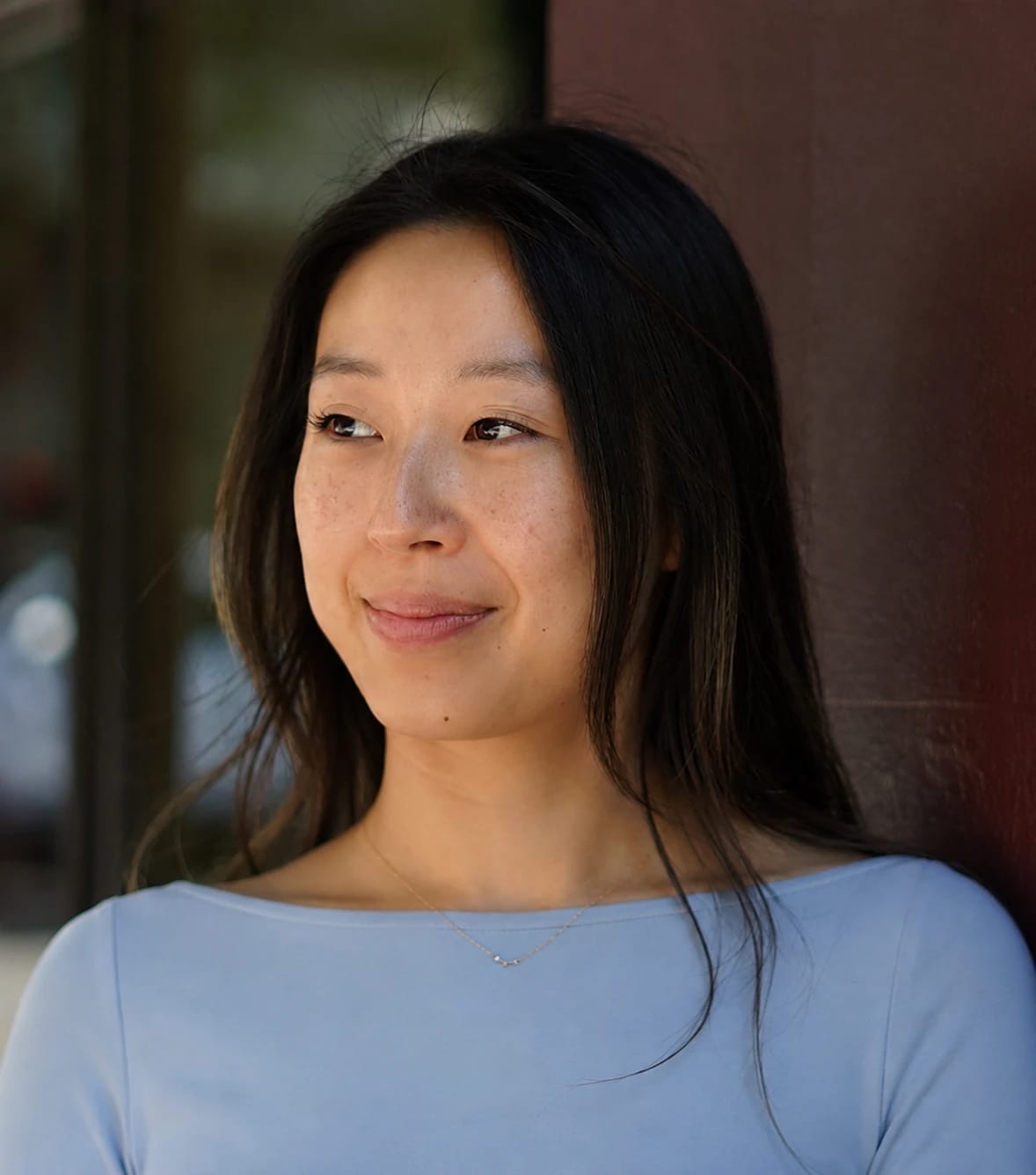 Portrait of a young woman with long dark hair wearing a light blue top.
