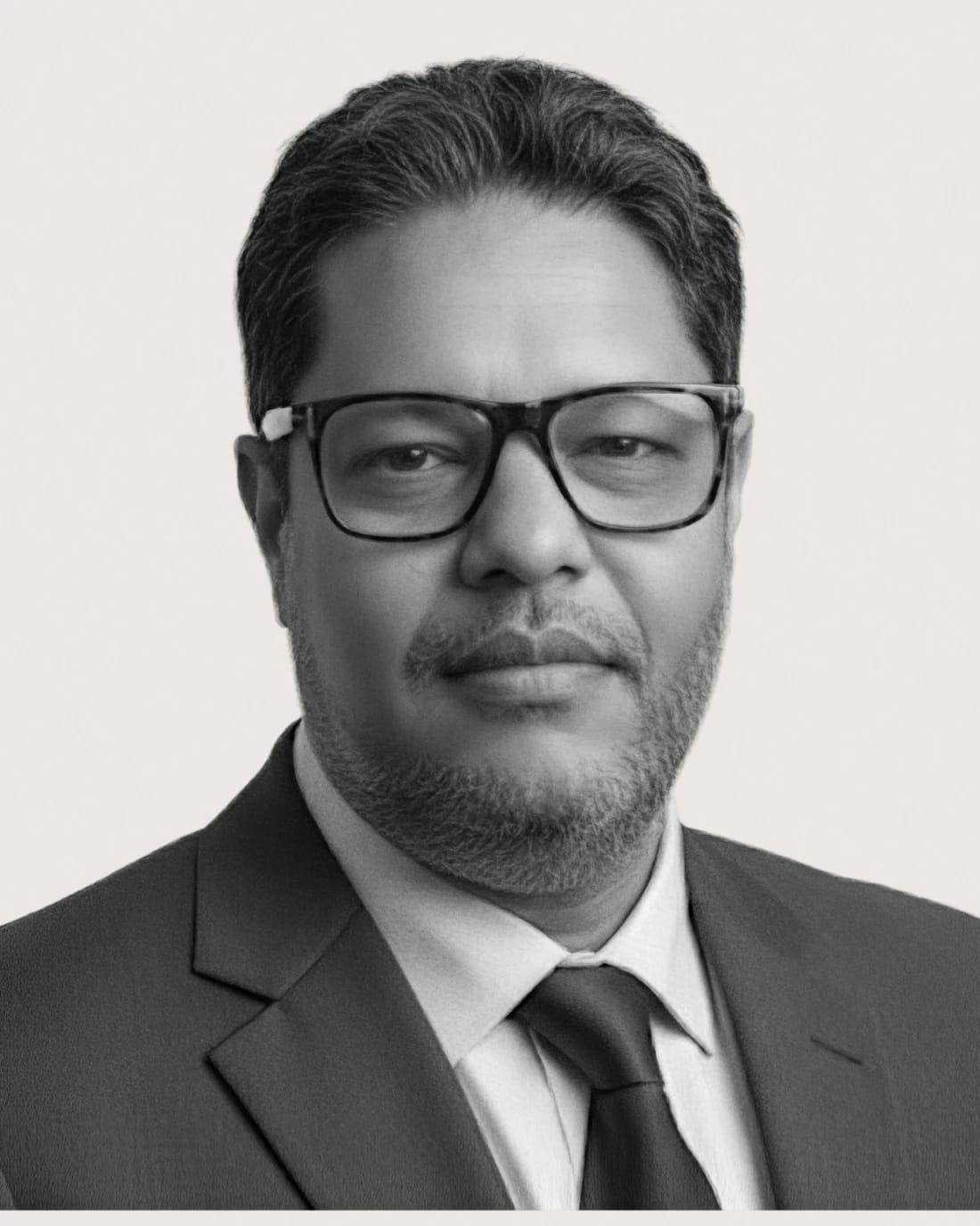 Headshot of an unidentified man wearing glasses, a suit, and tie.