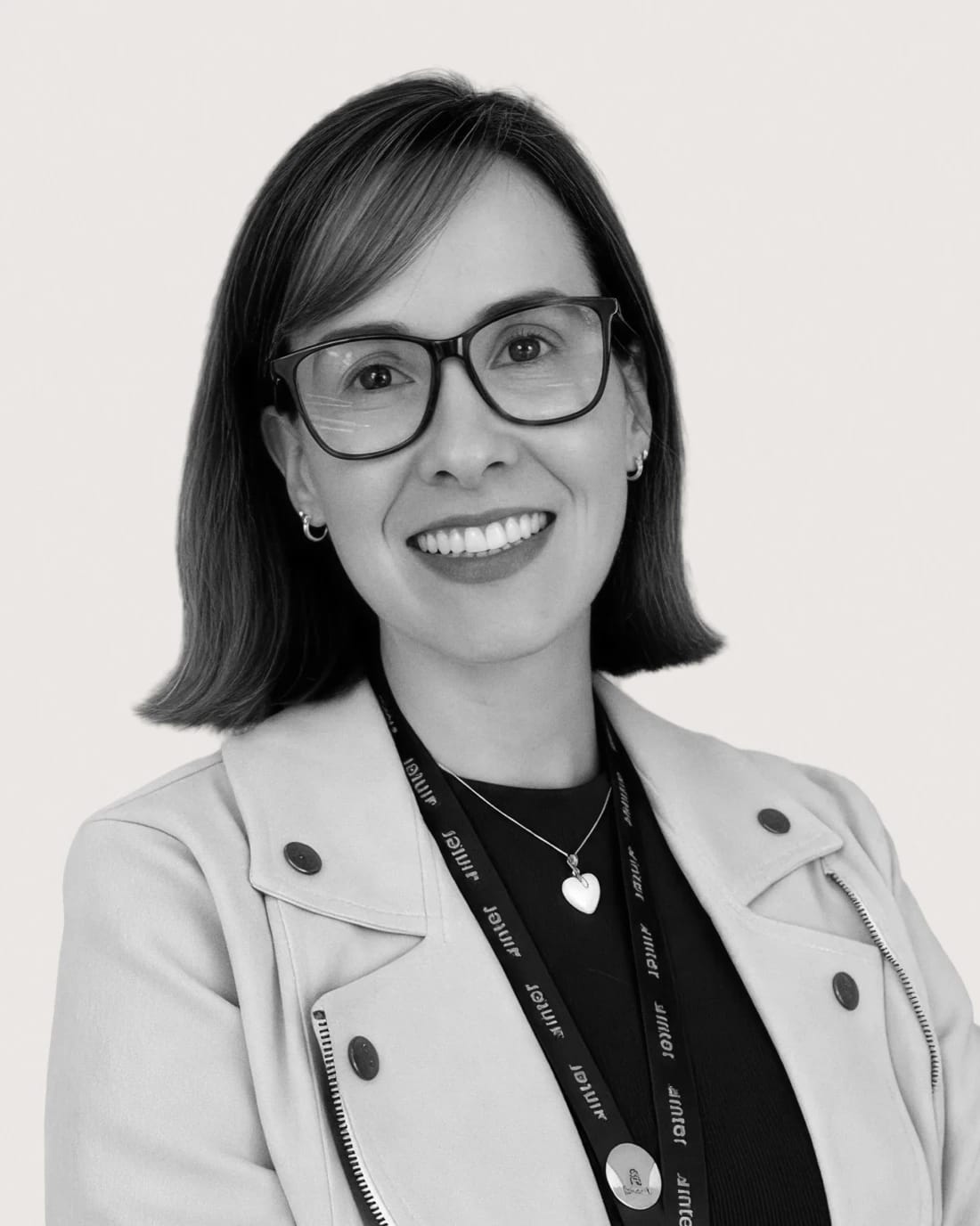 Smiling woman with glasses wearing a blazer and branded lanyard.