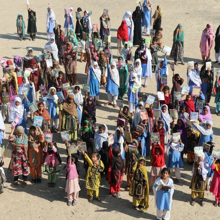 Children holding books outdoors in a large group.