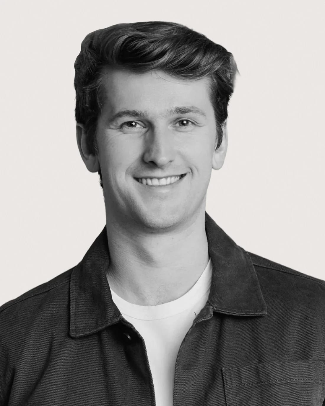 Smiling man in a white ElevenLabs T-shirt, shown in a grayscale portrait.