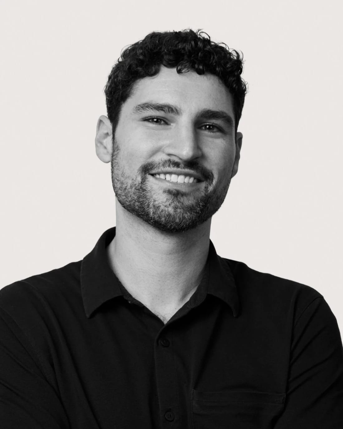 Smiling bearded man with curly hair wearing a black collared shirt.