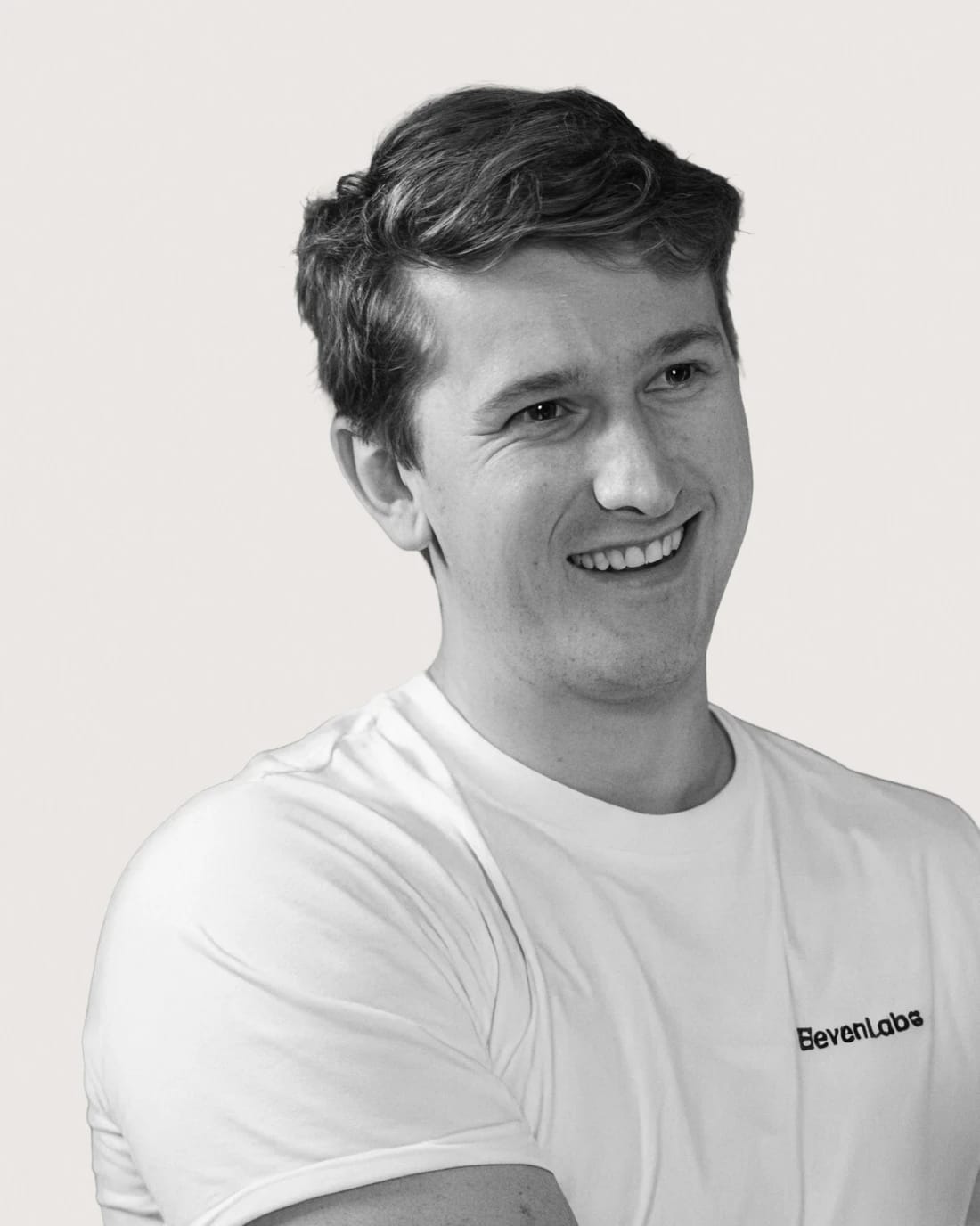 Smiling man in a white ElevenLabs T-shirt, shown in a grayscale portrait.