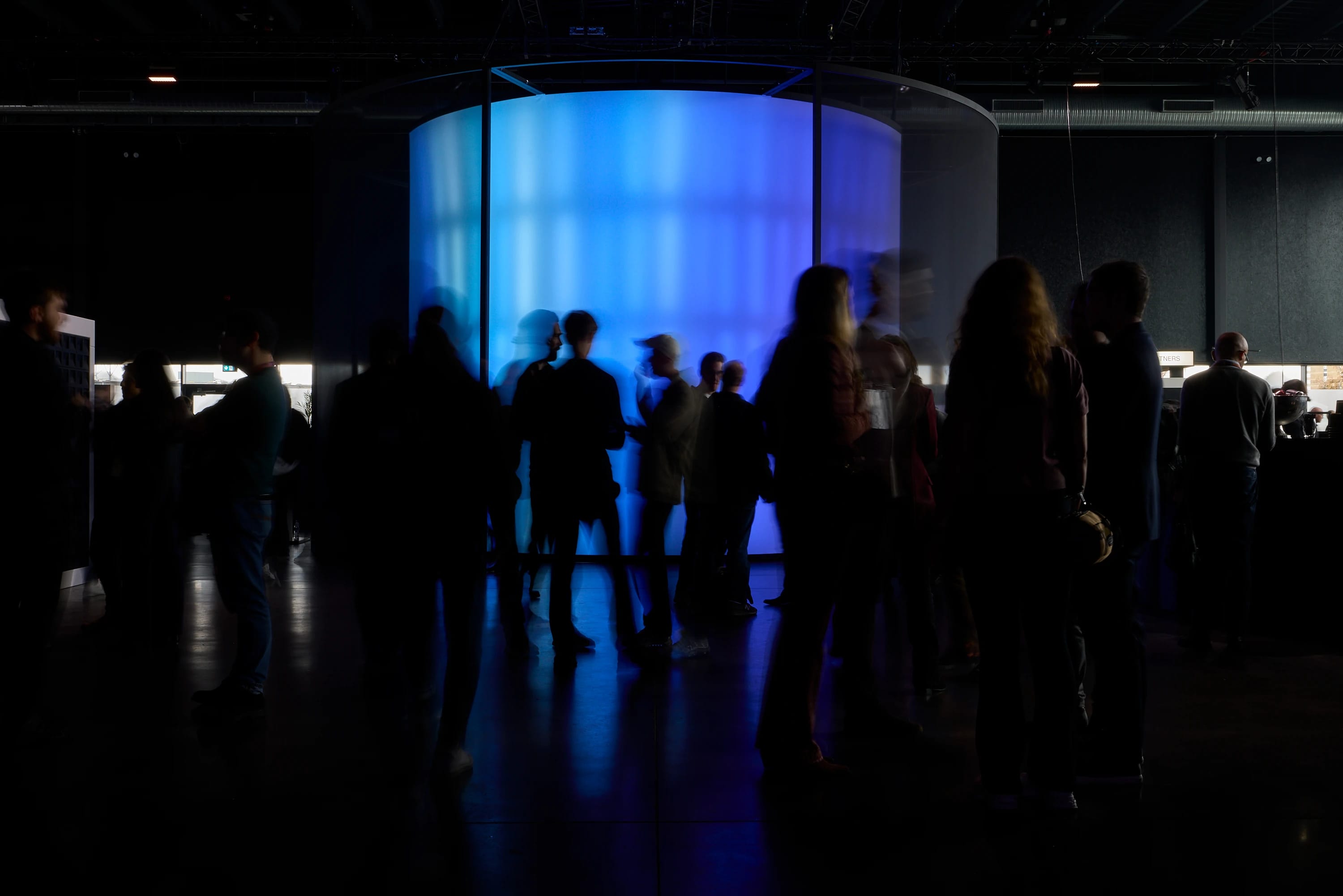 Attendees mingle in a dark event space beside a large blue illuminated installation.