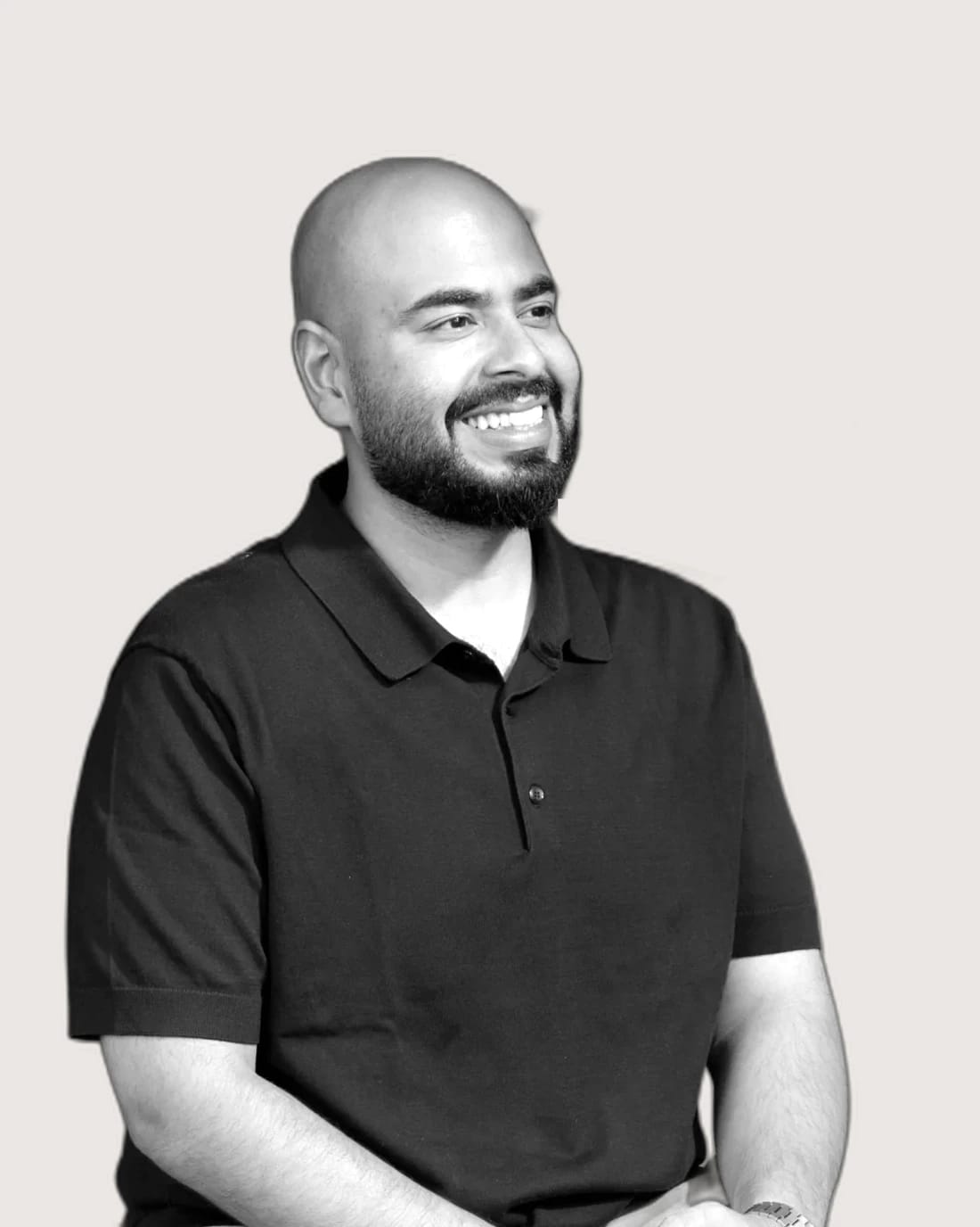 Smiling bald, bearded man wearing a black polo shirt.