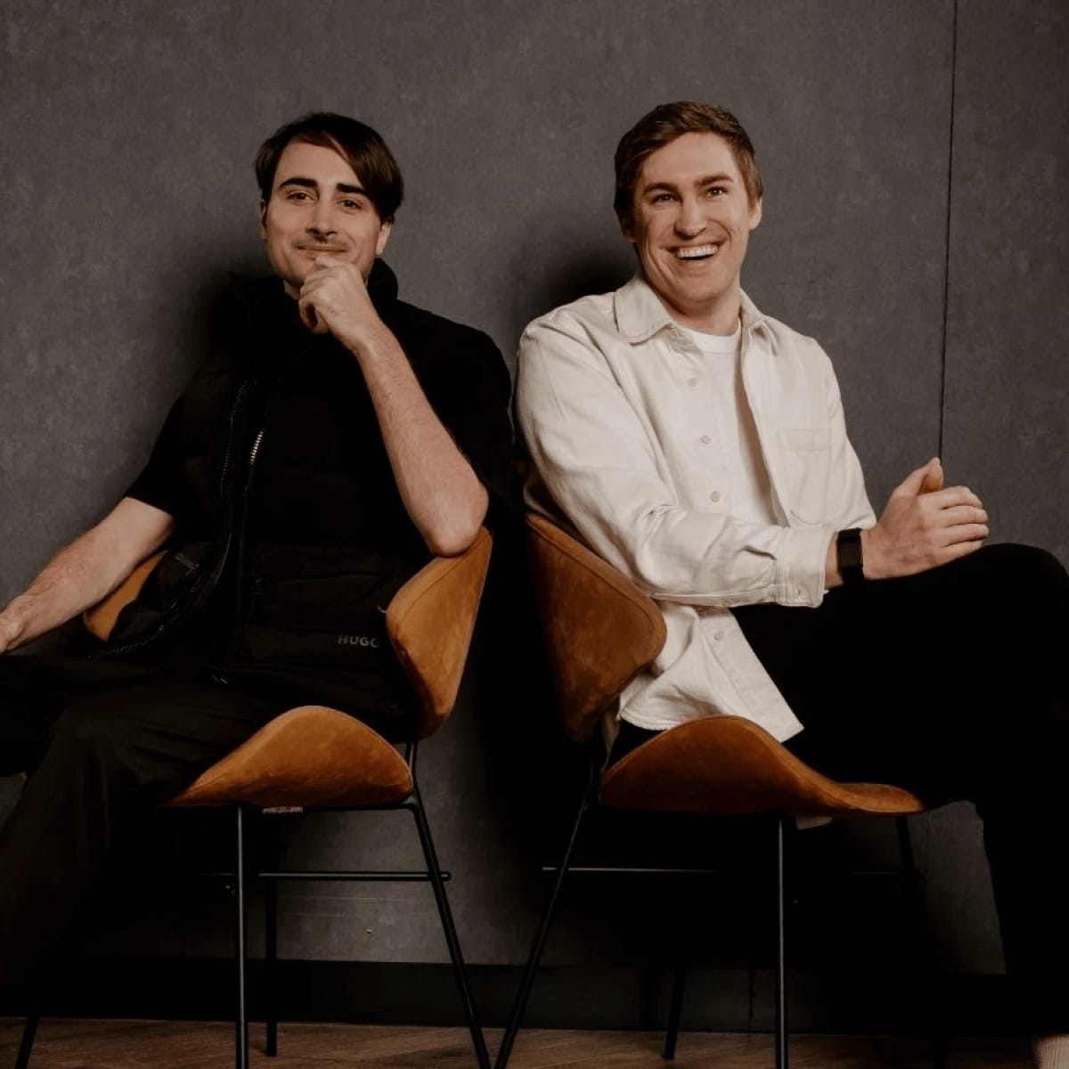 Two people seated, smiling; one in a white shirt, the other in a dark vest.