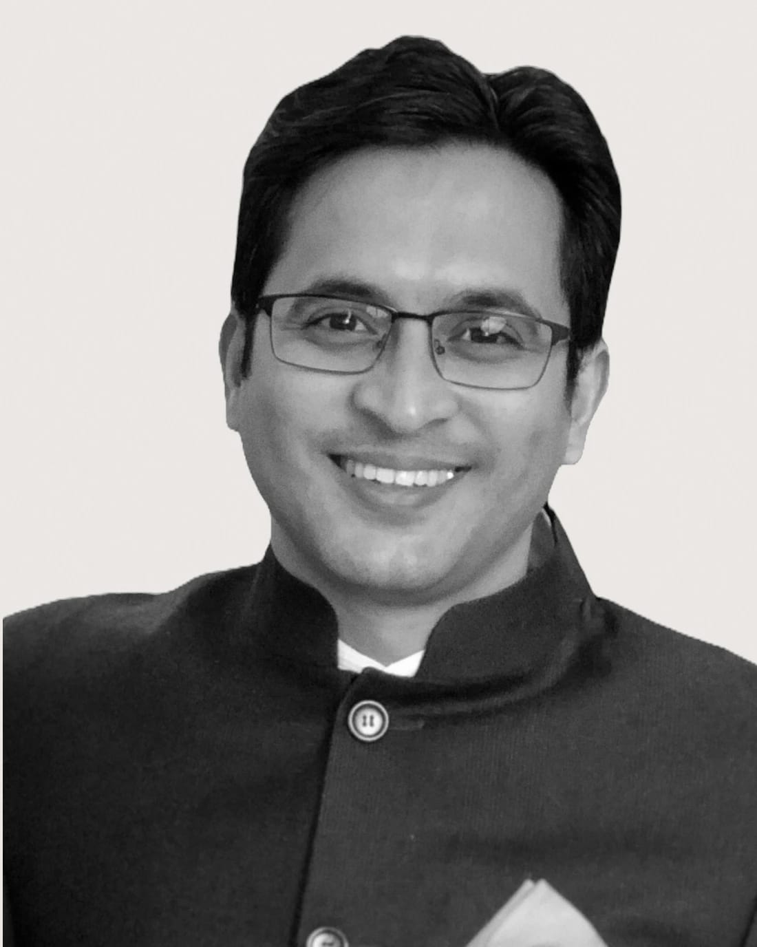 Smiling man wearing glasses and a dark formal jacket.