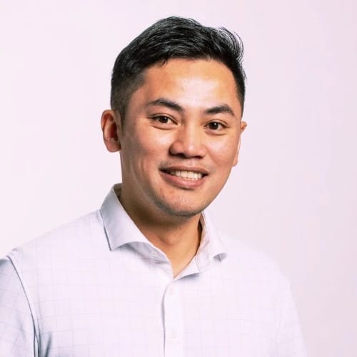 A person smiling in a white collared shirt against a plain background.