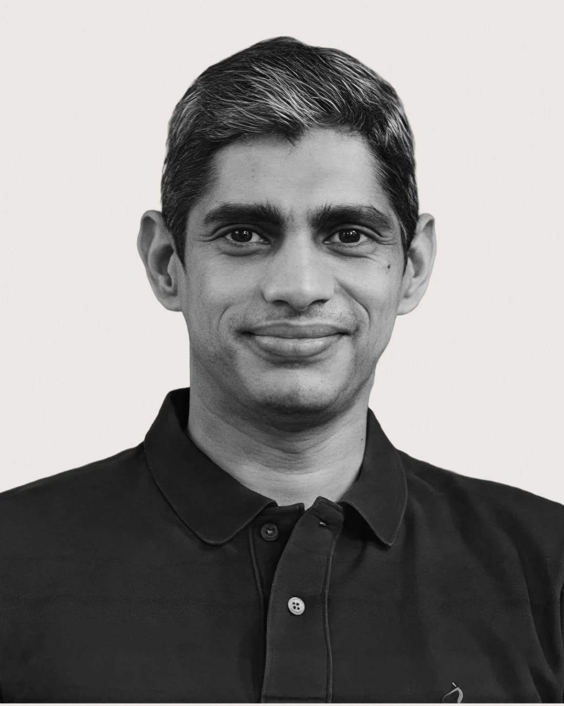 Black-and-white head-and-shoulders portrait of a smiling man in a dark collared shirt.