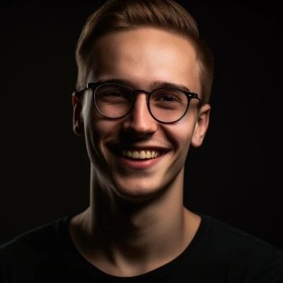 A young man with glasses smiling against a dark background.