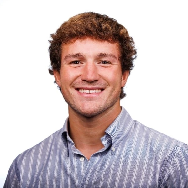 Smiling young man with curly brown hair wearing a striped button-down shirt.