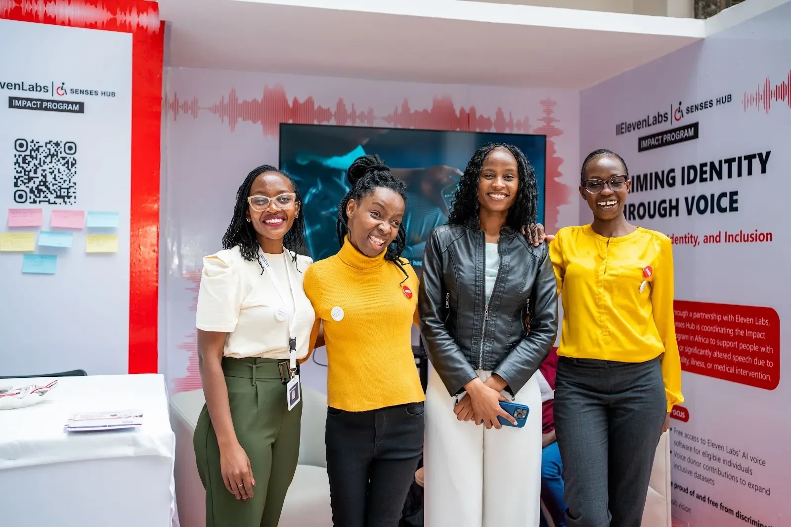 Four women stand together smiling with their arms around each other