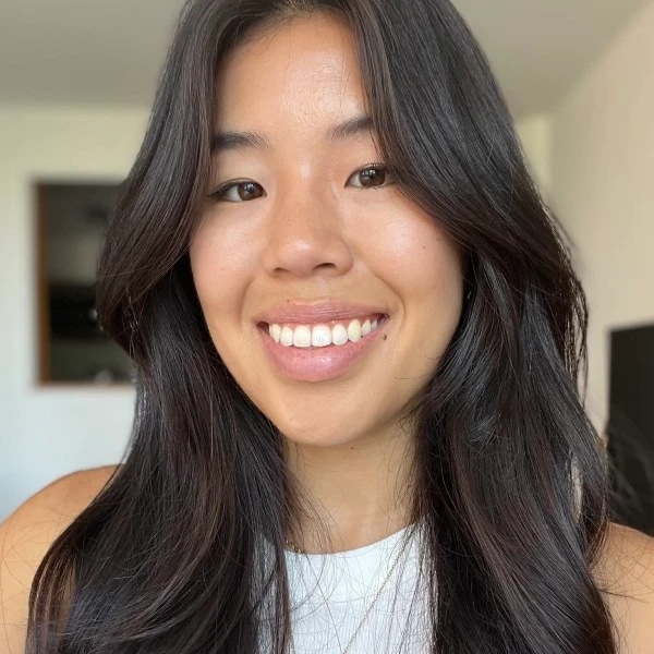Smiling person with long dark hair wearing a white top.