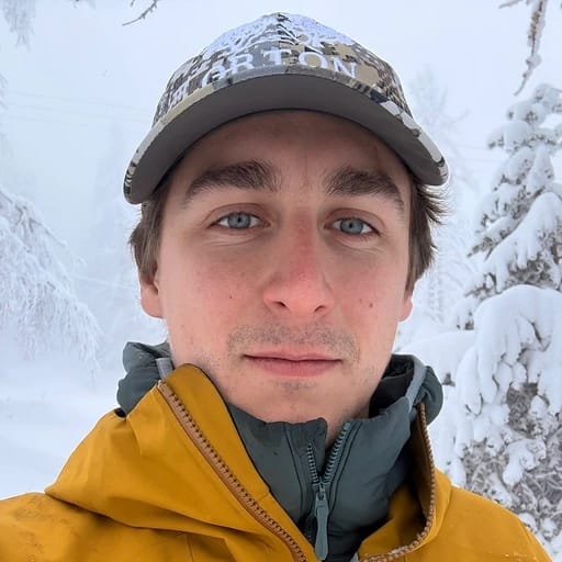 A person in a snowy landscape wearing a cap and yellow jacket.
