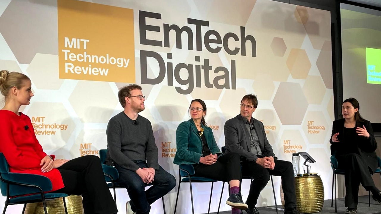 A panel of five people sitting on stage at the MIT Technology Review EmTech Digital event, engaged in a discussion.