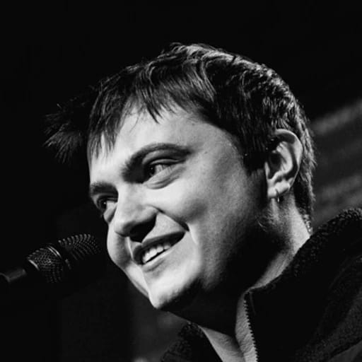 Close-up black-and-white portrait of a smiling singer performing into a microphone.
