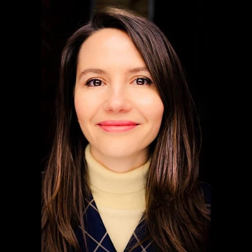 Smiling woman with brown hair, wearing a turtleneck and plaid jacket.
