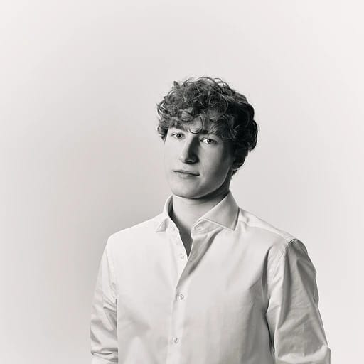 Young man with curly hair in a white shirt, looking slightly away in a black-and-white portrait.