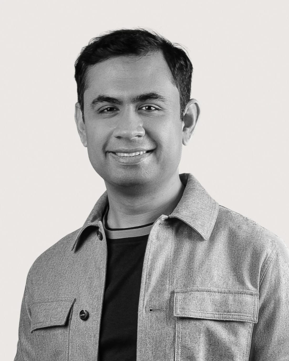 Smiling man wearing a gray overshirt over a black shirt.