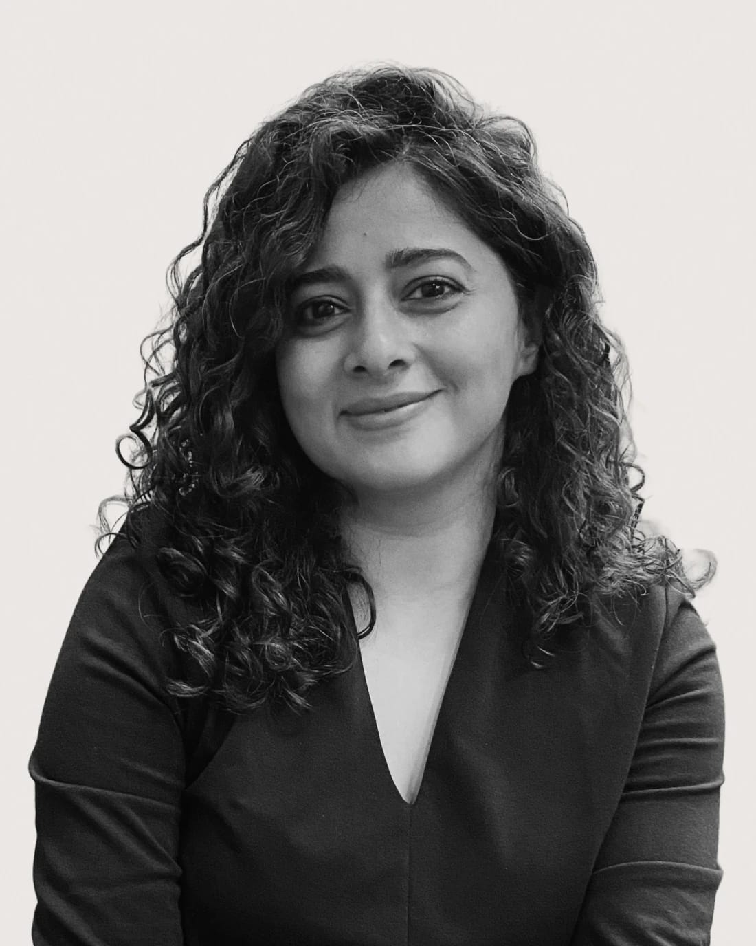 Smiling woman with curly hair wearing a dark V-neck top.