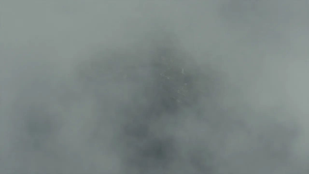 30-second cosmic horror movie trailer, 1990s theatrical style, complete with title cards. Character A: a marine biologist in her 40s, salt-crusted parka, chapped face, deep exhaustion in her eyes. Character B: an old harbor master in his 70s, milky left eye, oilskin coat, trembling hands. Setting: a decaying fishing village on a black ocean, thick fog, crooked docks, a dead lighthouse. Structure: Cold open (0-4s): slow aerial descent through fog toward the village, the ocean unnaturally still, a vast dark shape suggested beneath the surface; low drone building. Beat one (4-9s): quick cuts, abandoned boats, nets dropped mid-haul, a meal still steaming on a crate, the biologist walking the empty dock; whispered voice-over tone. Title card (9-11s): black screen, white serif text: 'THIS SUMMER'. Beat two (11-17s): the harbor master grabs her arm and points at the water; the tide pulls back too far, too fast, exposing monolithic carved stones that should not exist; thousands of seabirds flee inland. Title card (17-19s): black screen: 'SOME THINGS SLEEP'. Beat three (19-25s): accelerating montage, the fog glowing sickly green from below, villagers running, the lighthouse flickering back to life on its own, the biologist screaming something we cannot hear, waves rising; music swelling then cutting to silence. Final card (25-28s): title reveal in weathered serif letters: 'THE DEEP BELOW', text slowly warping as if underwater. Stinger (28-30s): one last shot, the ocean surface, calm, then a colossal eye opens just beneath it; hard cut to black with a deep boom. Trailer editing grammar: rhythmic cuts synced to sound design, dread through suggestion, the creature never fully shown until the final stinger. Desaturated cold palette with sickly green undertones, heavy fog diffusion, 35mm film grain, deep sub-bass rumble, distant foghorn.