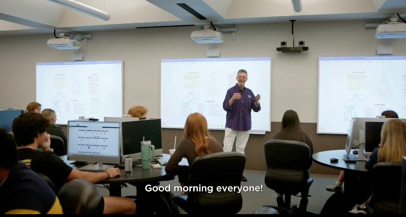 Instructor welcomes students in a computer classroom with lecture slides displayed.