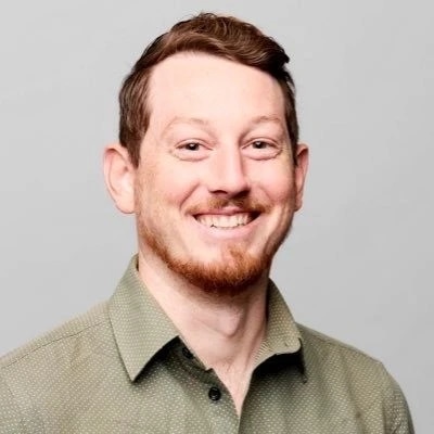 A smiling man with short brown hair and a beard, wearing a green collared shirt.
