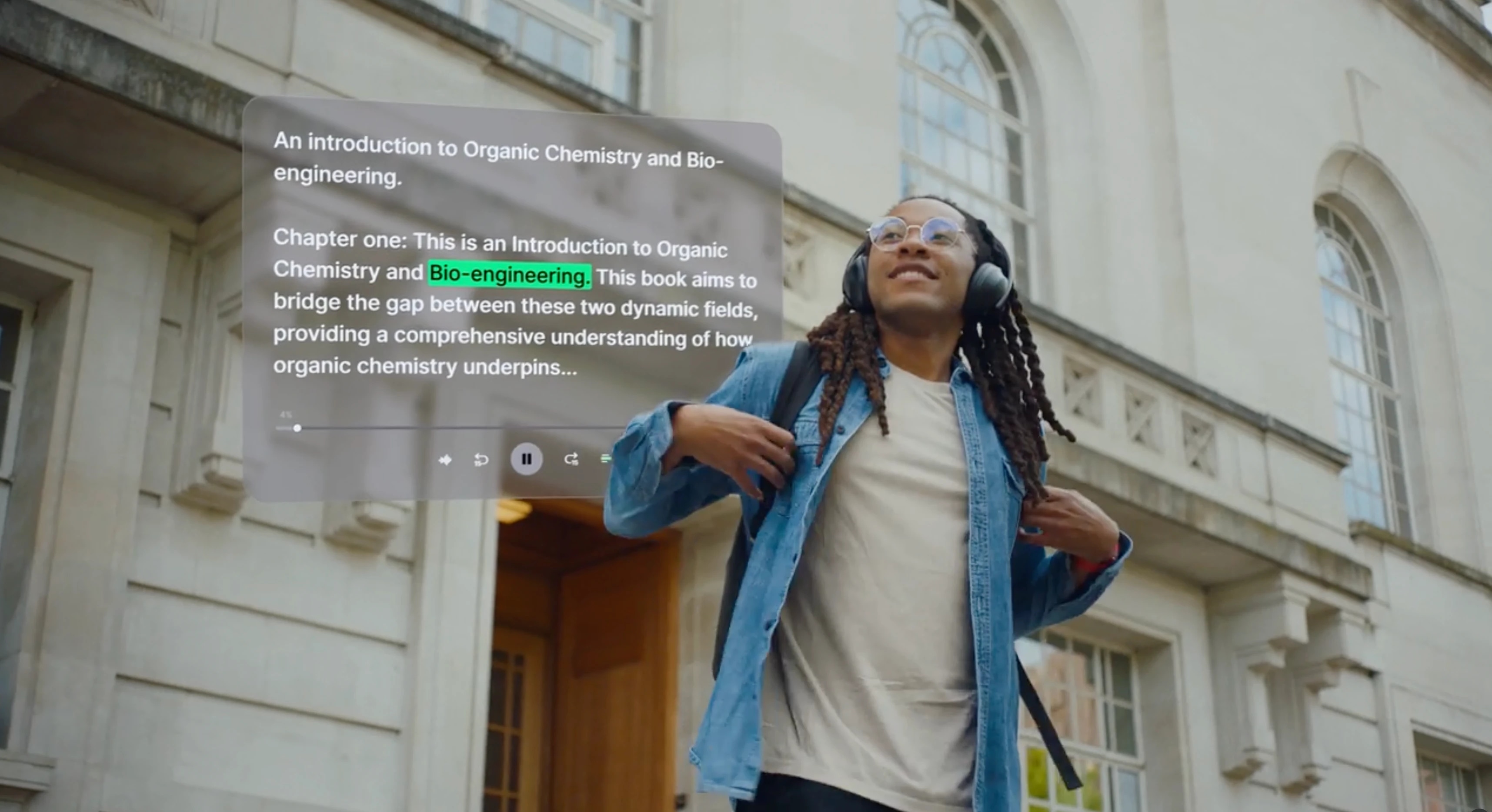 A person with glasses and headphones standing outside a building, looking up with a backpack on their shoulder.