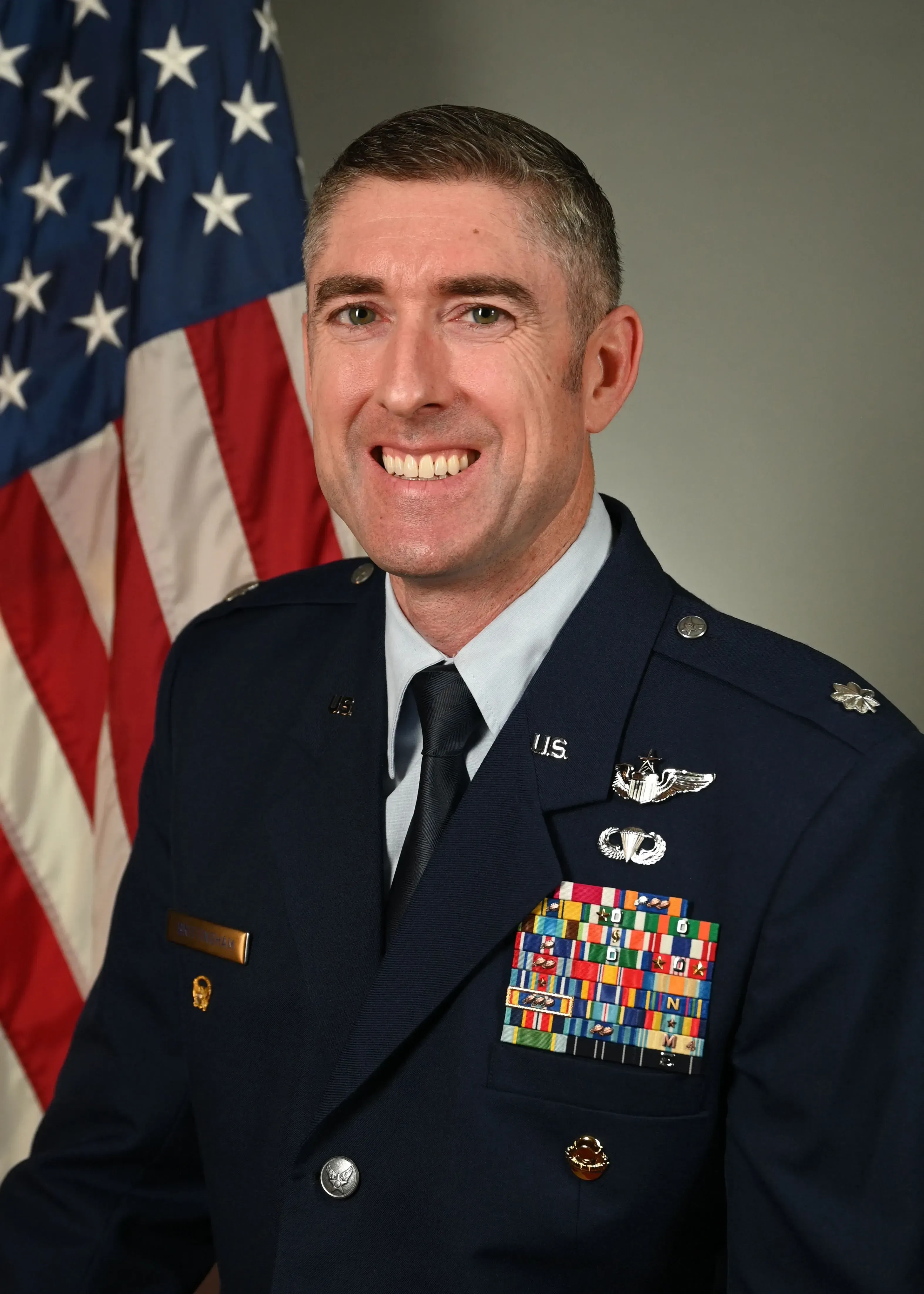 Lt Col Thomas Brittingham in his U.S. Air Force uniform, smiling in front of the American flag.